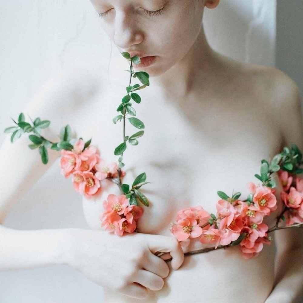 Femme aux seins nus pâle avec des bouquets de fleurs remontant ses seins