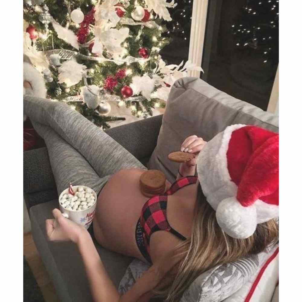 Fille enceinte mangeant des biscuits pour le dîner devant l'arbre de Noël